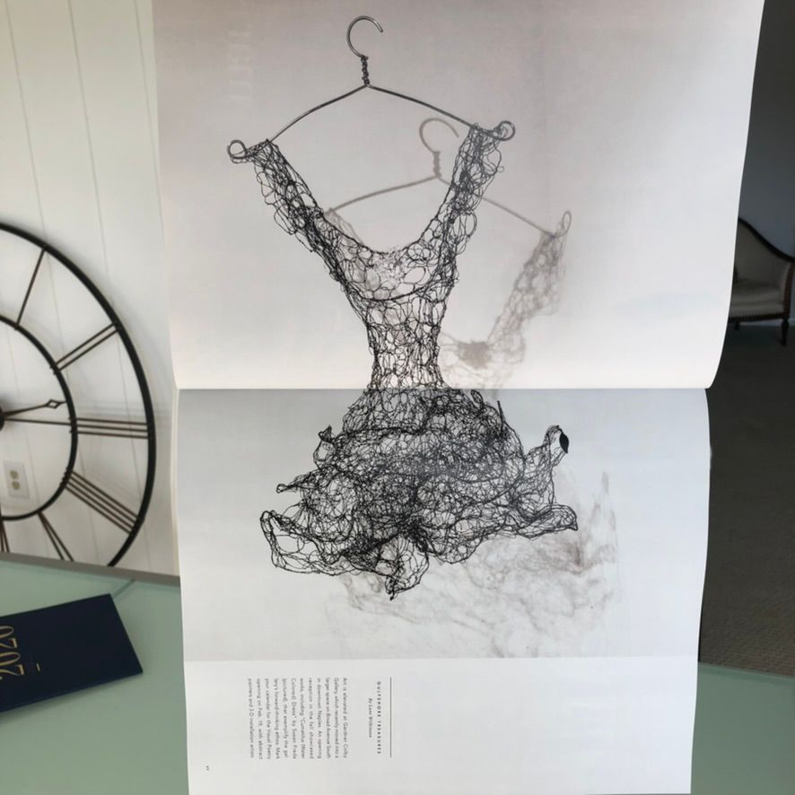 Intricate wire sculpture of a dress on a hanger displayed in a magazine spread, with a clock visible in the background.