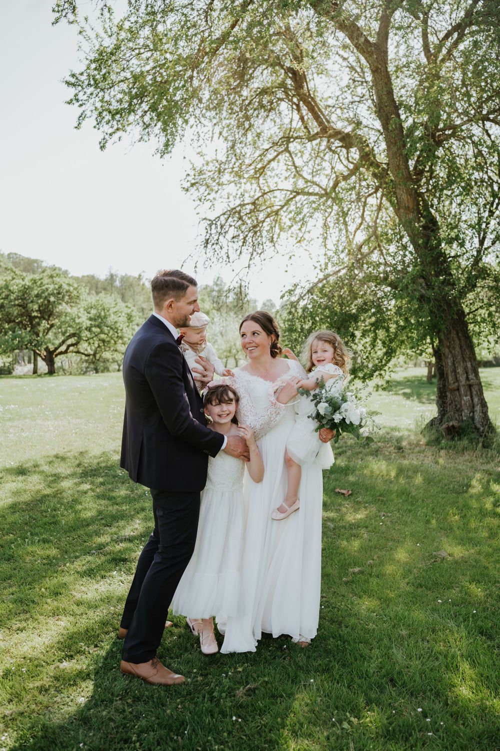 A wedding party poses together under a blooming tree on a sunny spring day in a grassy field.