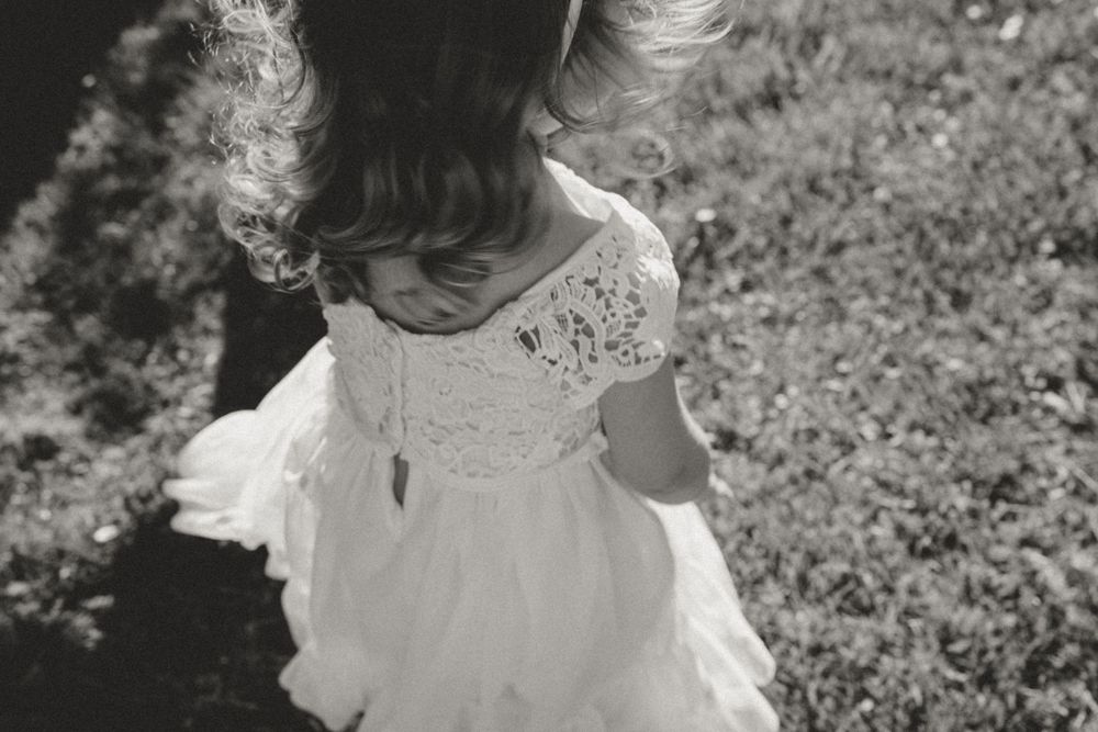 A black and white portrait of a twirling flower girl in a lace dress.
