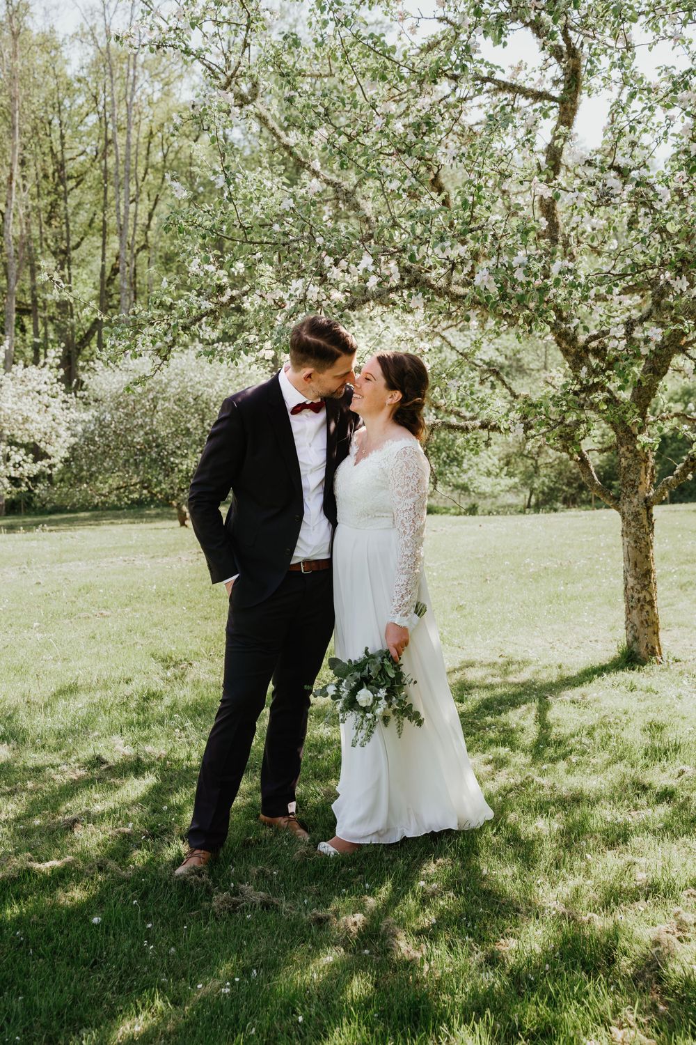 A romantic spring wedding portrait under blooming trees in a garden setting.
