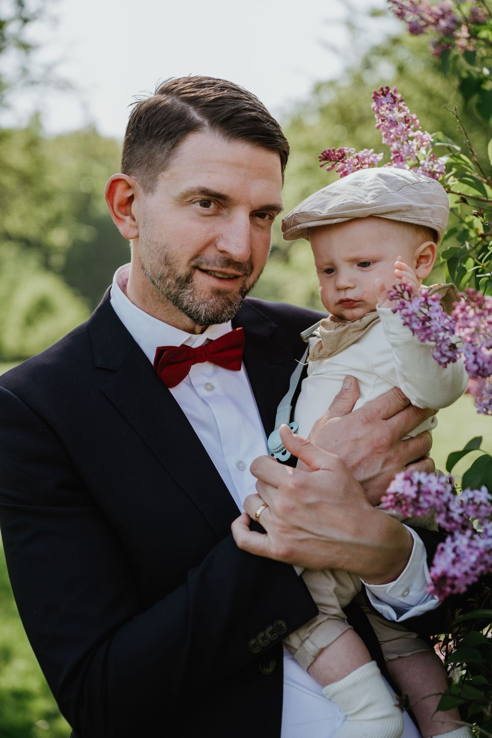 An outdoor springtime wedding portrait beside blooming lilac bushes.