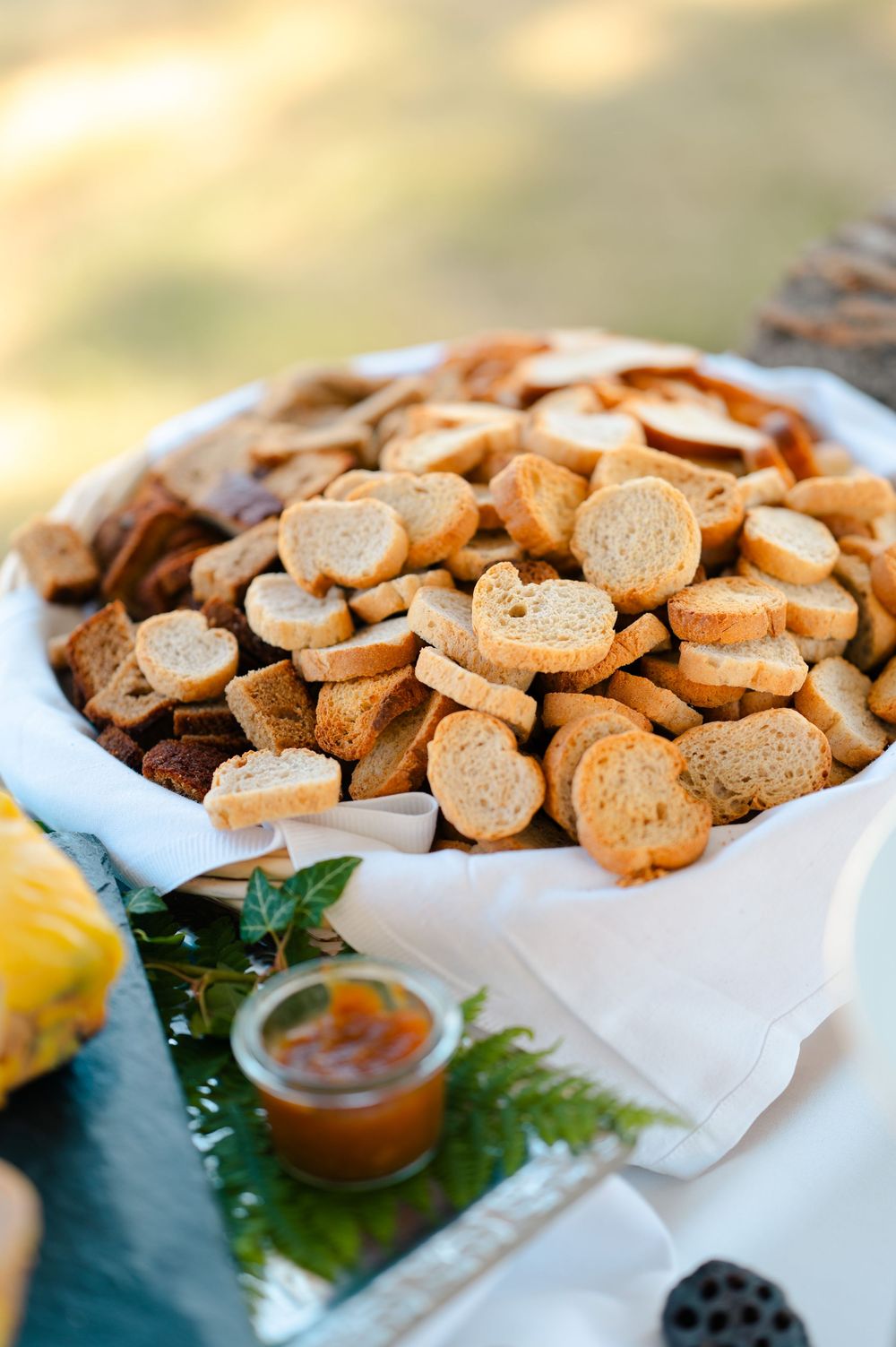 A platter of toasted baguette slices served with lemon and a small bowl of sauce on decorative leaves.