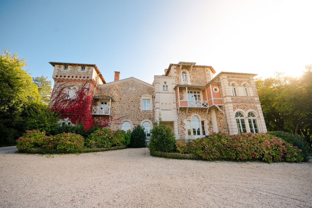 Panoramic view of a grand historic mansion with stone facade and landscaped grounds at sunset.