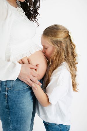 Tender mother-daughter maternity moment captured against white background in casual attire. Maternity photographer.
