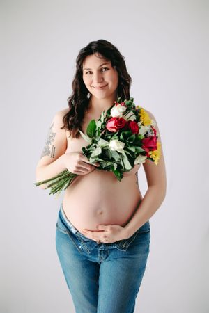 Artistic maternity photo series showing a woman in jeans holding colorful roses against a white backdrop. Middle TN maternity photographer.
