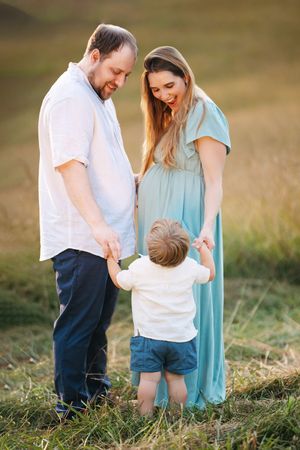 A family in white and blue outfits shares tender moments together in a grassy outdoor setting during golden hour.