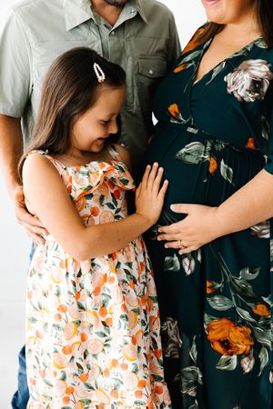 A couple embraces tenderly in a romantic photoshoot, with her wearing a floral dress and him in dark clothing.