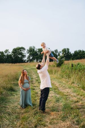 A couple in a grassy field shares joyful moments during a maternity photo session in nature.