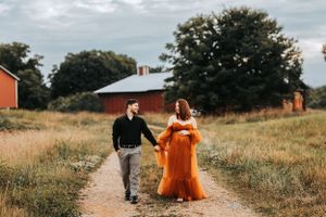 Couple walking down rural path with orange dress flowing in countryside setting. Middle TN Maternity Photographer