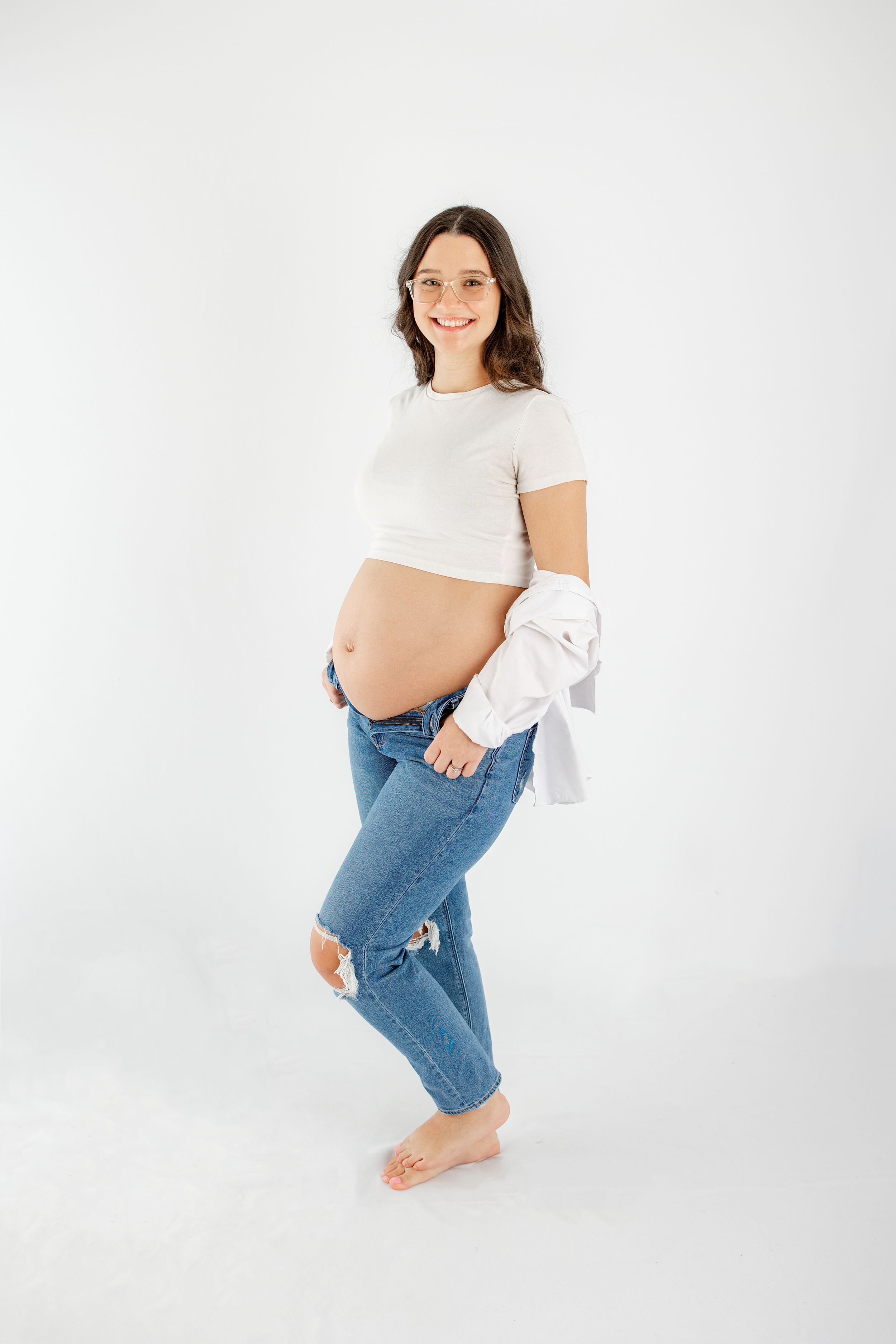 Woman in casual white top and blue jeans poses against white background in minimalist studio photoshoot.