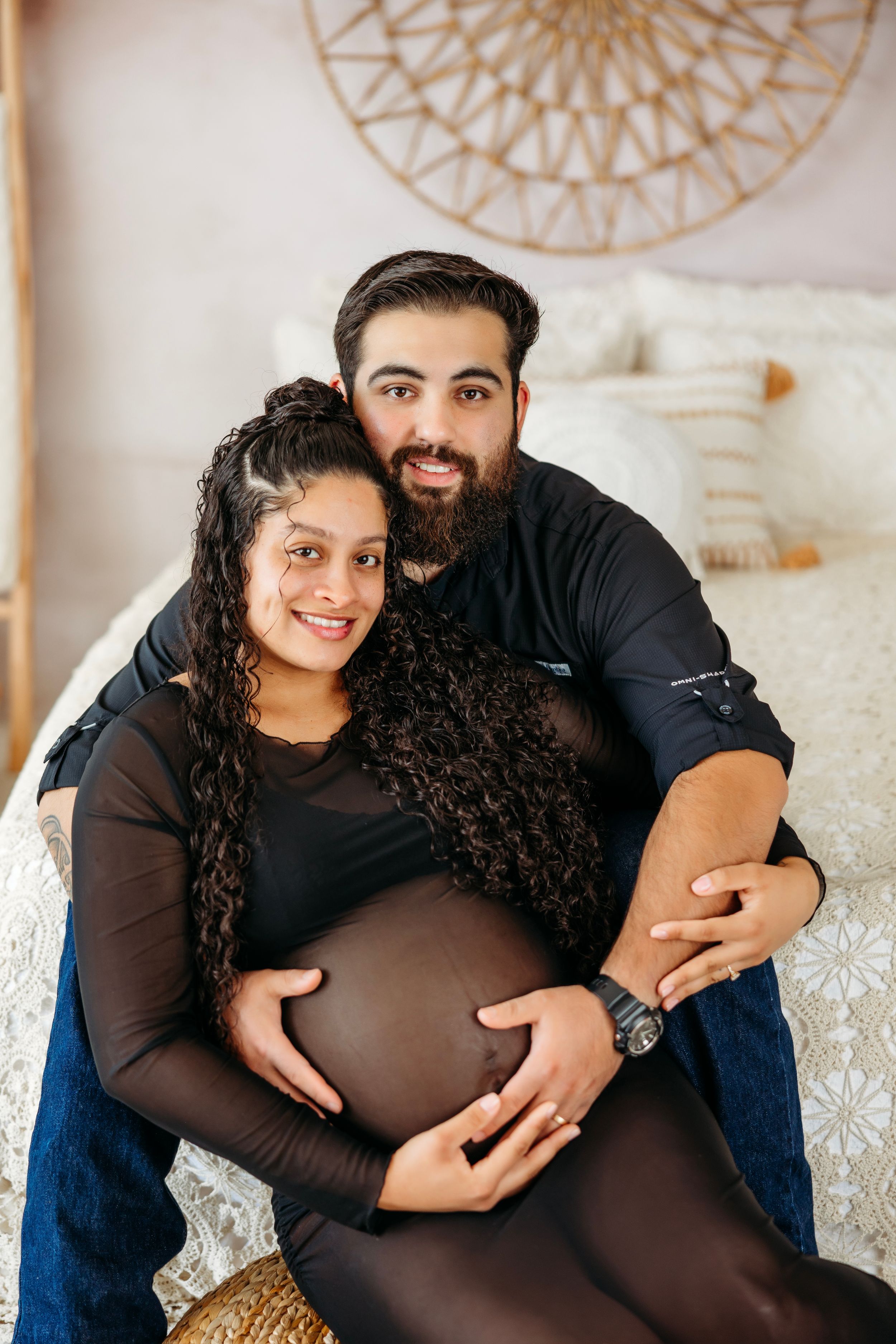Maternity photos on white background featuring couple in black attire with decorative wall art. Middle TN Maternity Photographer