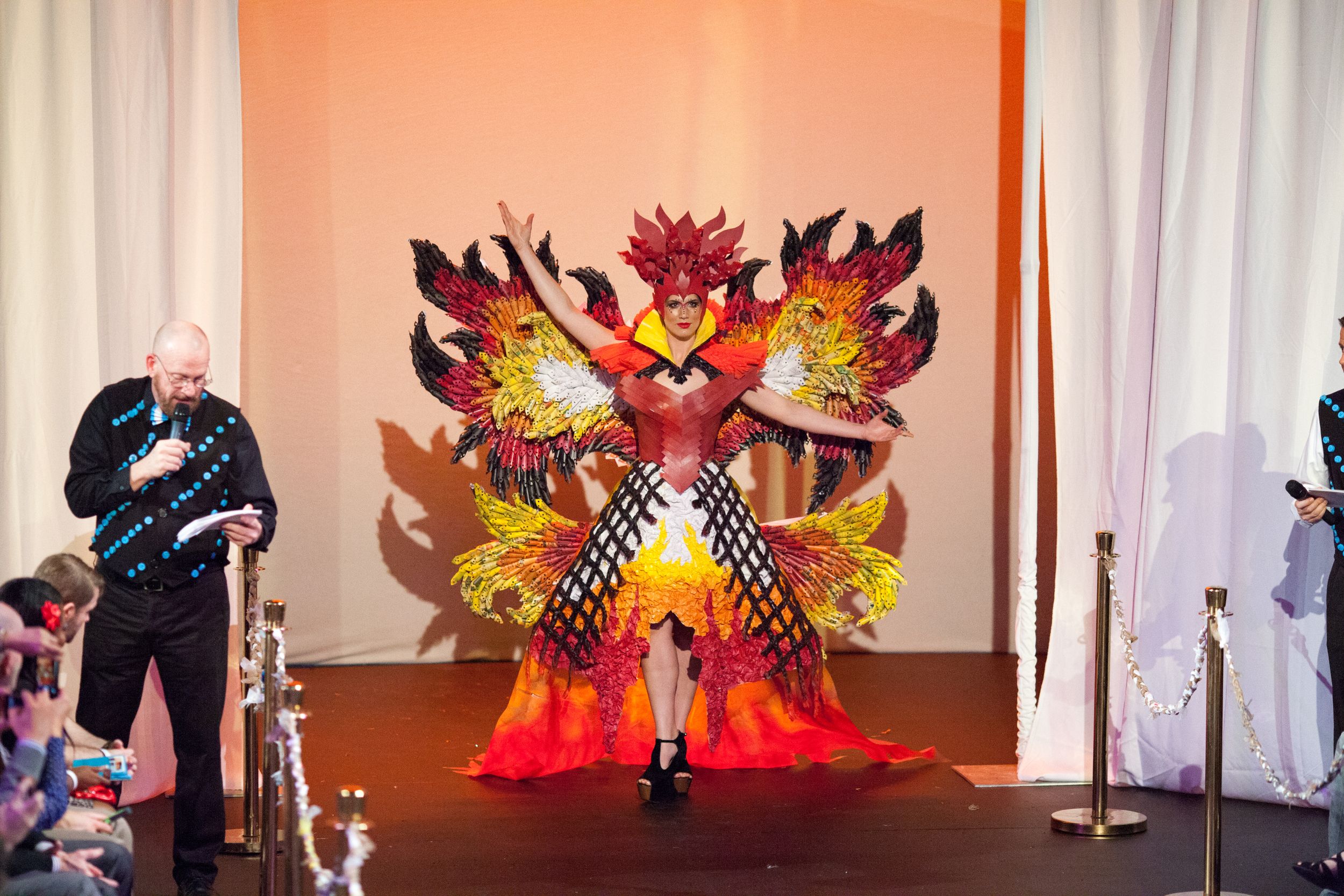 Fiery phoenix-inspired costume with dramatic wings displayed on illuminated runway.