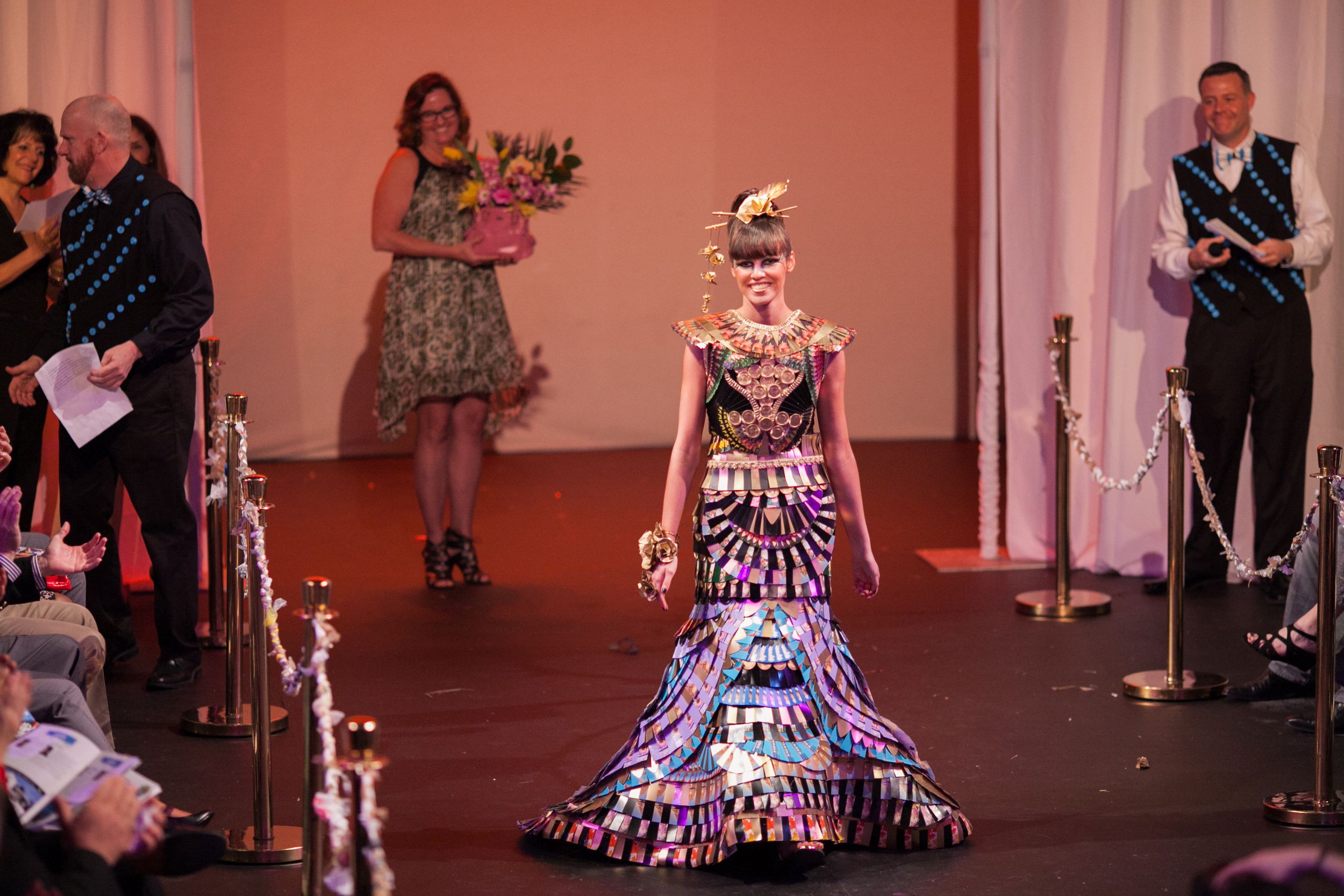 Performer in illuminated LED dress stands center stage during theatrical production.