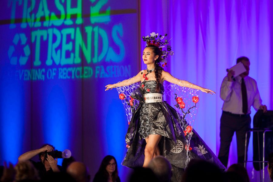 Model performs in avant-garde dress made from recycled materials at fashion show with dramatic lighting.