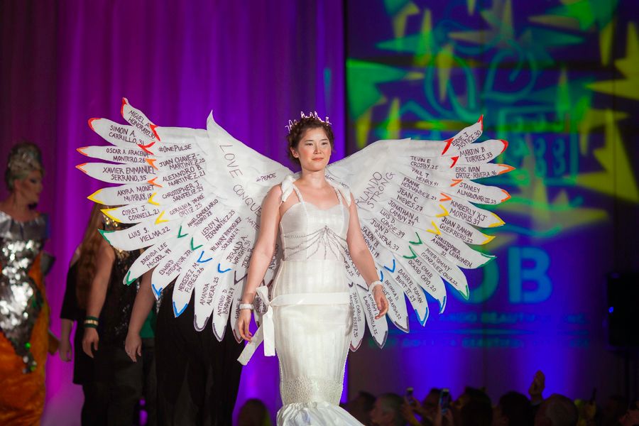 Dramatic white recycled angel wings costume displayed on runway with colorful stage lighting.