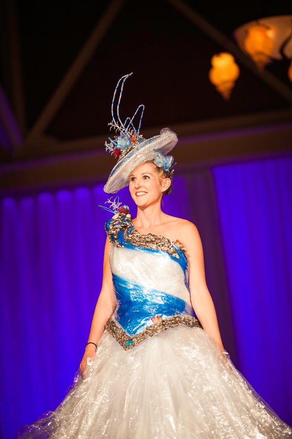 Model wears ethereal blue and white gown with sculptural hat at recycled fashion show.