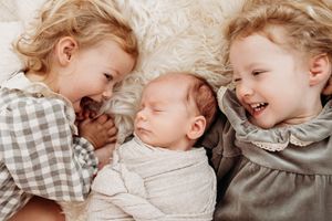 big sisters laugh with tiny newborn baby brother sibling newborn photography