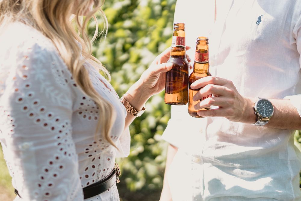 Close-up of hands toasting with beer bottles in sunlit vineyard setting.