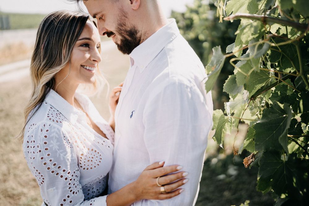 Intimate moment between couple wearing white and light blue in vineyard setting.