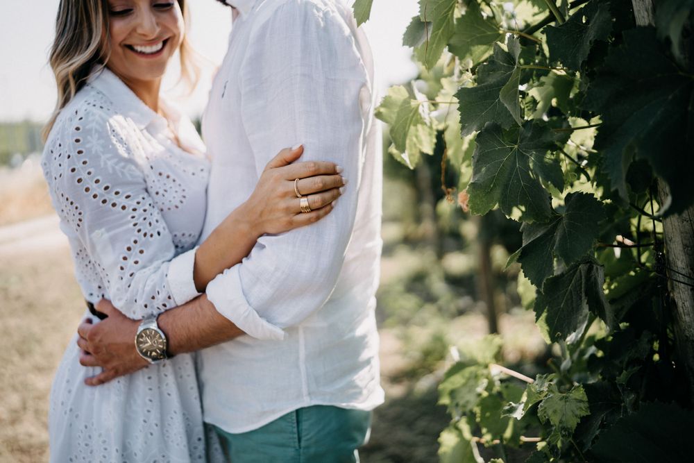 Close-up shot of couple embracing among grapevines in a sun-lit vineyard.