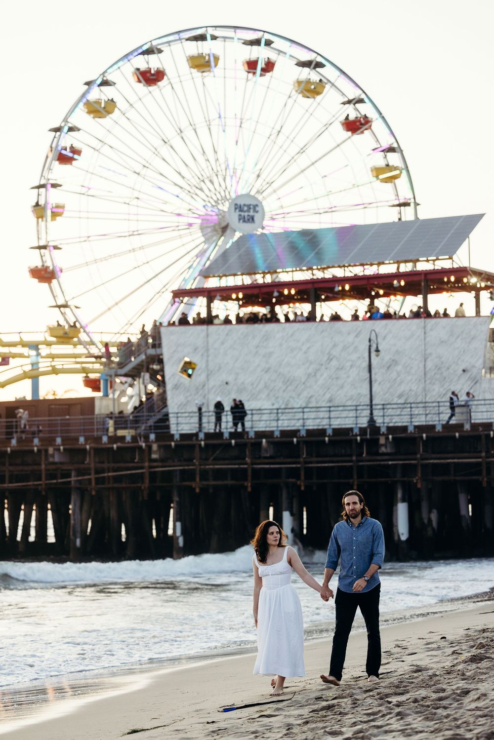Beach scene with iconic Santa Monica Pier Ferris wheel in the background at sunset.