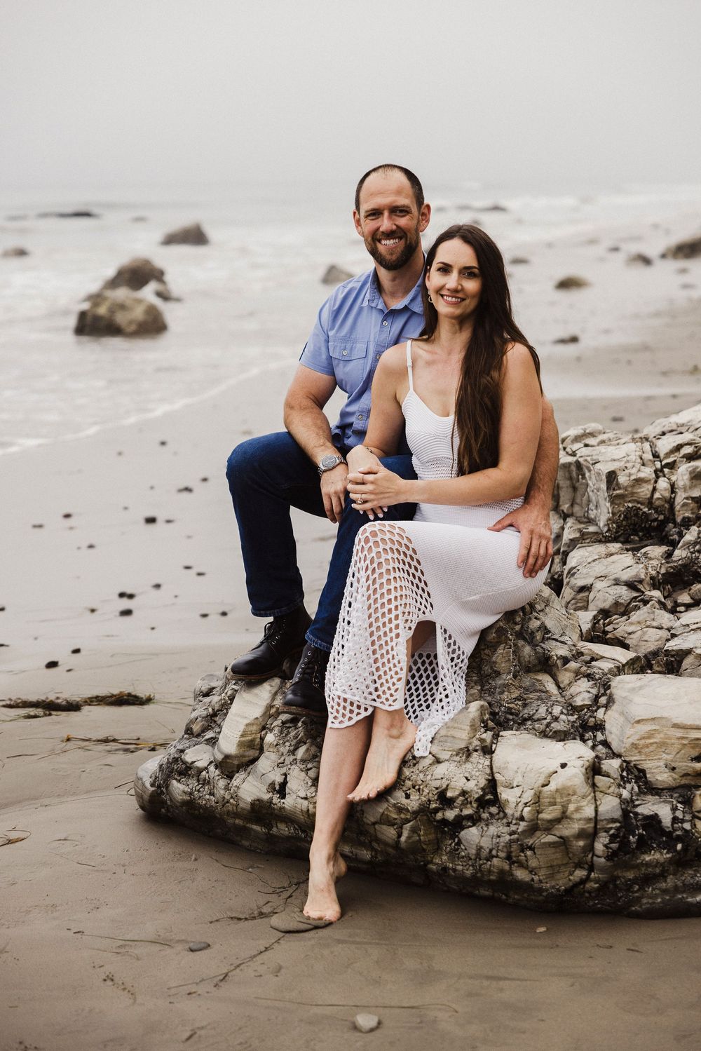 Couple relaxing on coastal rocks at a misty beach.