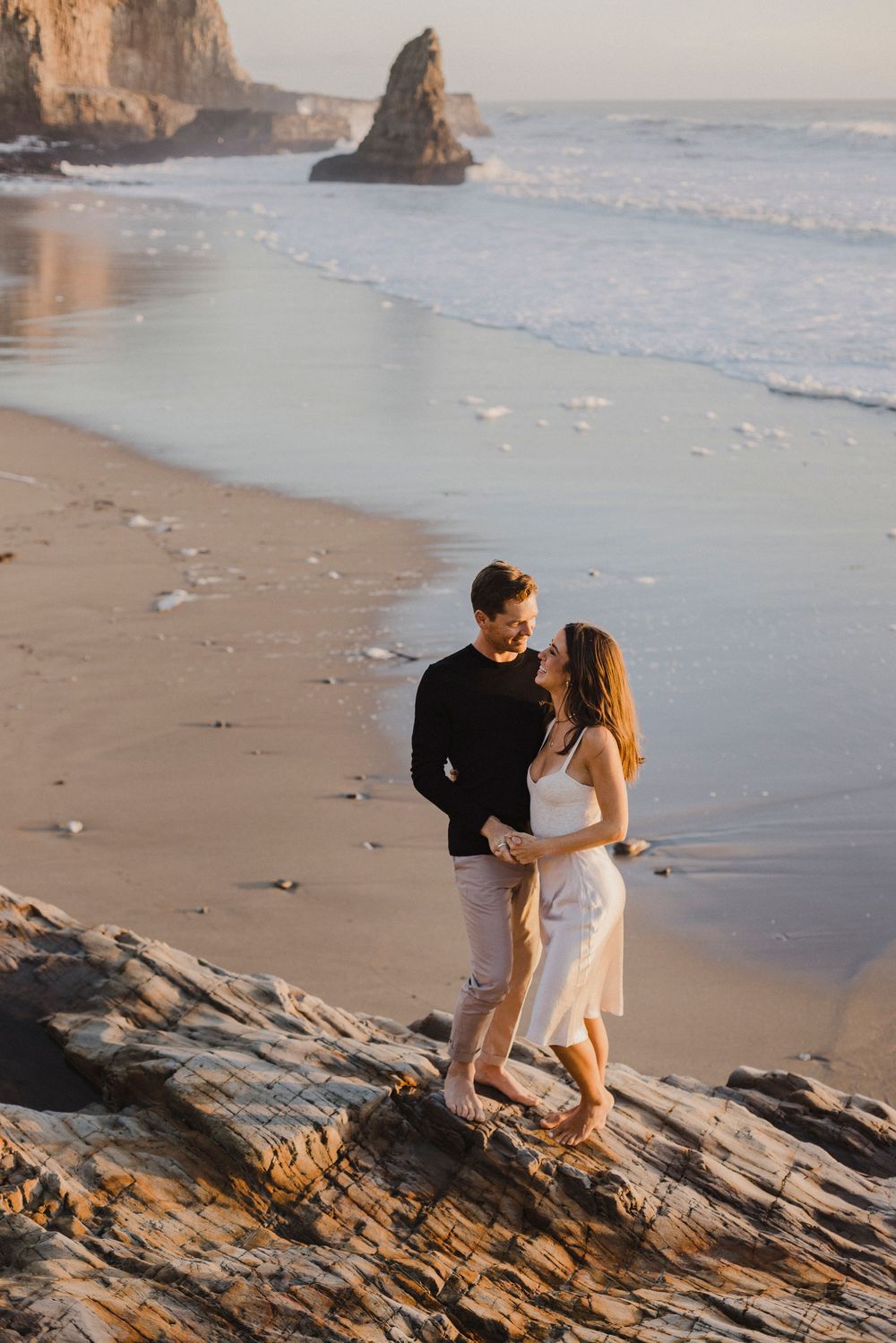 A couple shares an intimate moment on rocky coastal cliffs during golden hour.
