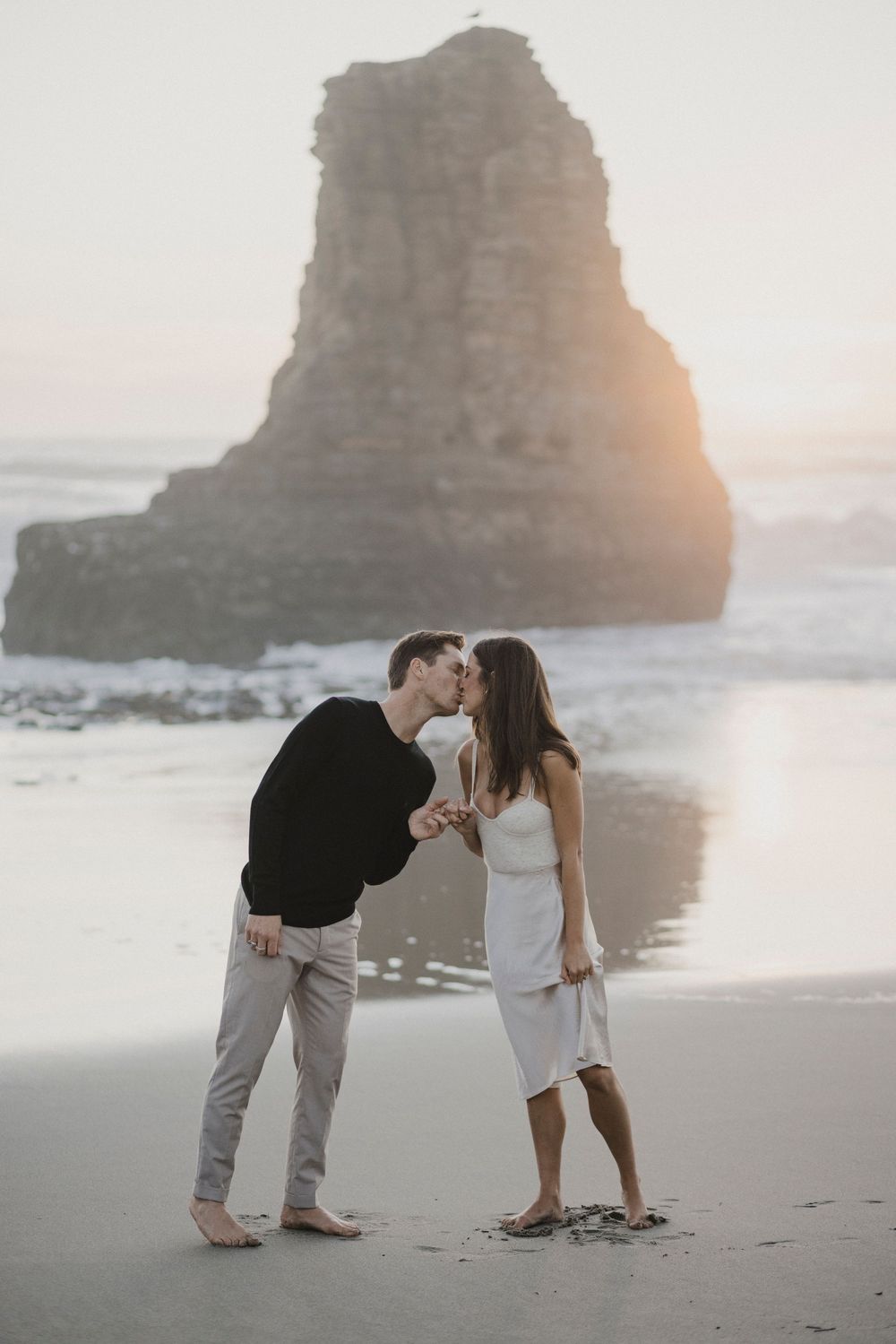A romantic moment shared between two people on a beach with sea stacks and gentle waves.