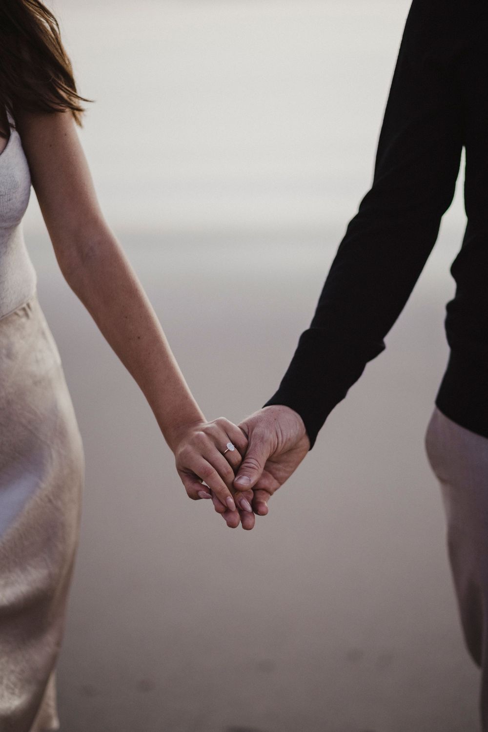 Close-up shot of hands reaching for each other on a misty beach at sunset.