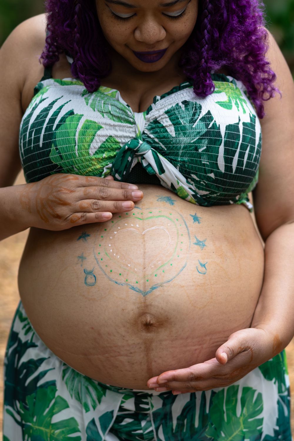 A pregnant belly adorned with body art wearing a tropical print swimsuit top.