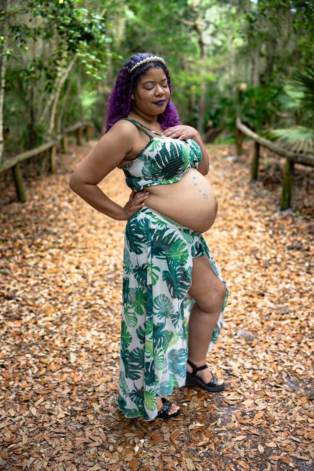 A maternity photo on a wooded trail wearing a tropical print dress.