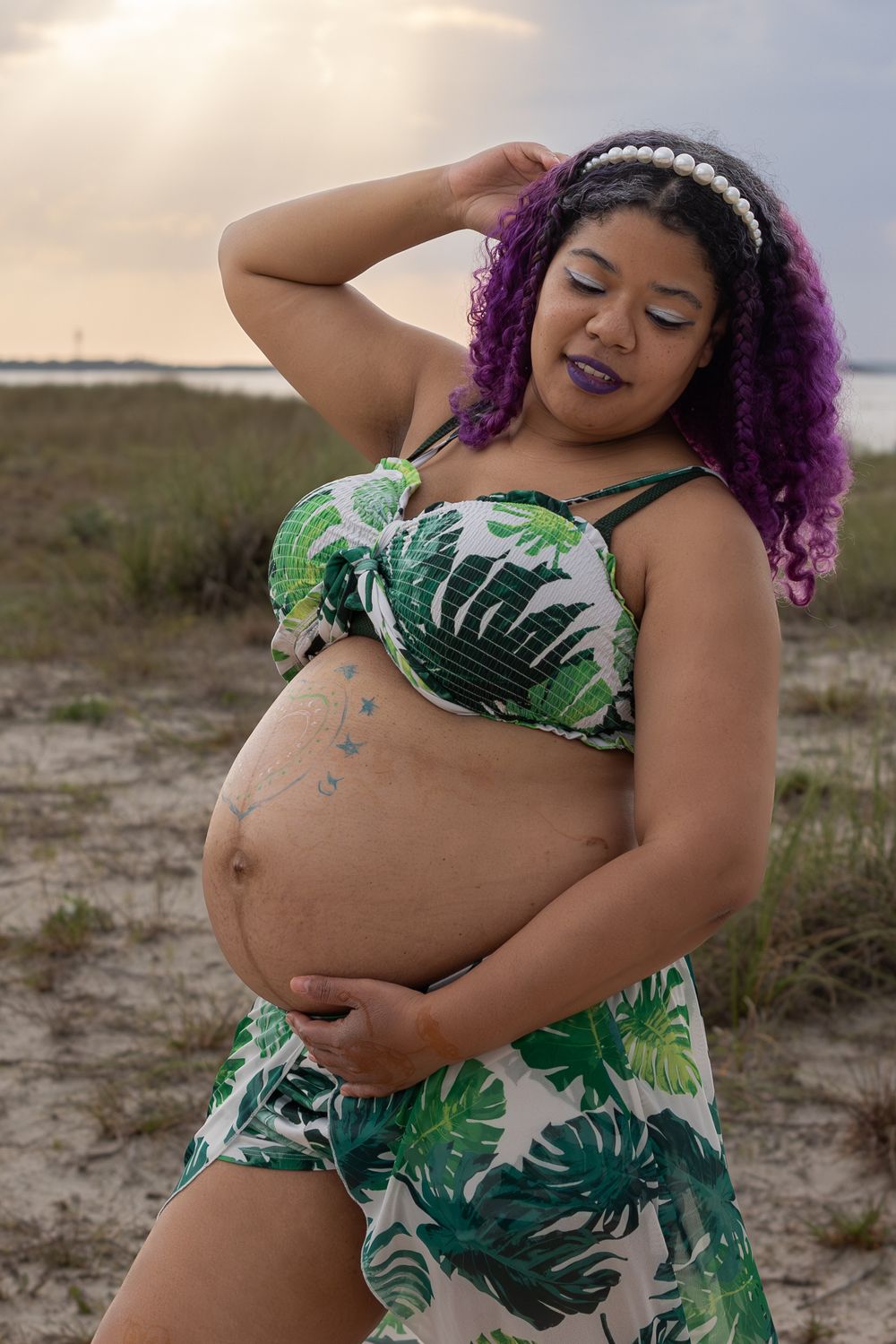A maternity photo shoot featuring a tropical print outfit against a sunset backdrop.