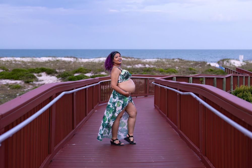 Person in tropical dress posing on a wooden boardwalk with ocean view.