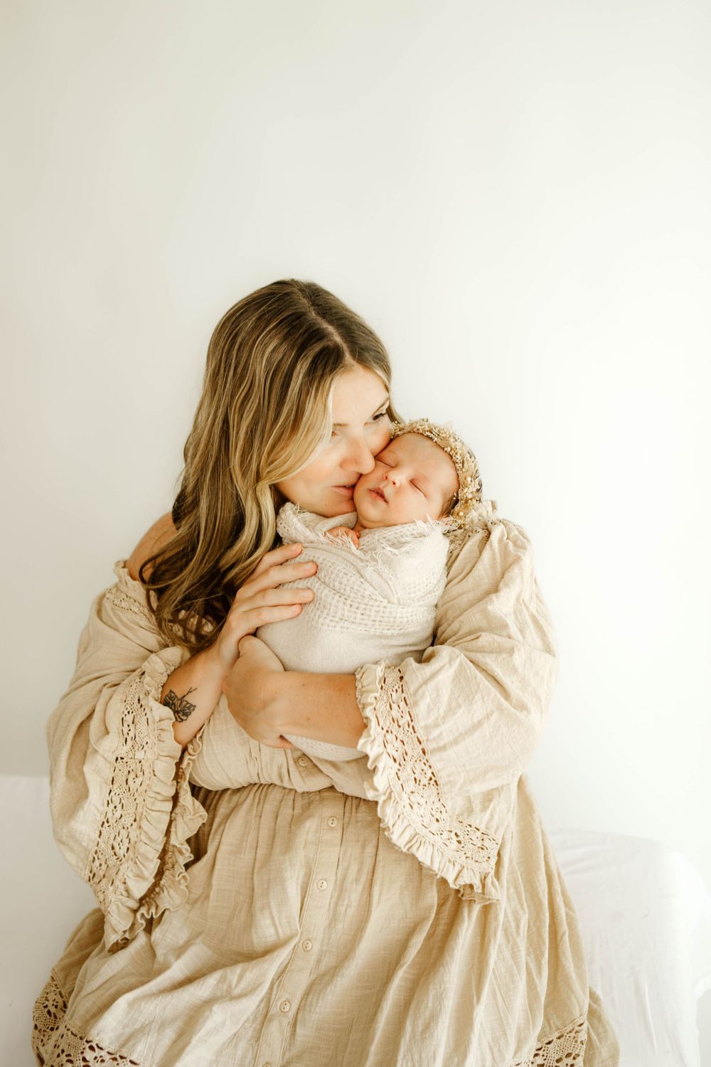 Tender moment captured in soft natural light with cream-colored lace dress against white background.