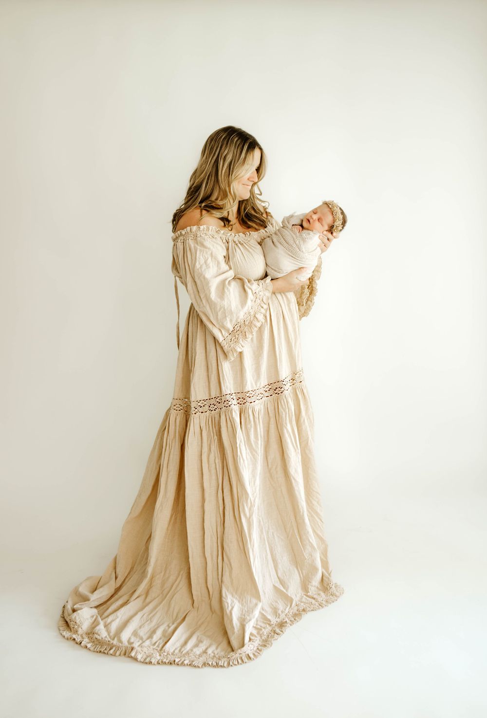 Elegant off-shoulder cream dress with lace details photographed against minimalist white backdrop.