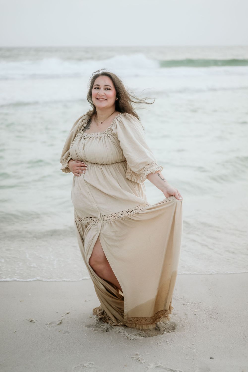 Ethereal beige dress flows in the ocean breeze as waves crash on a sandy beach during a seaside photoshoot.