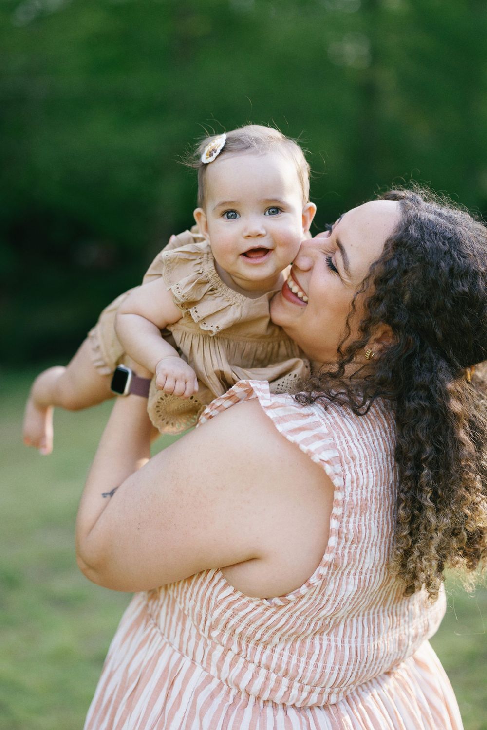 Sweet moment between parent and baby in ruffled outfits against green background.