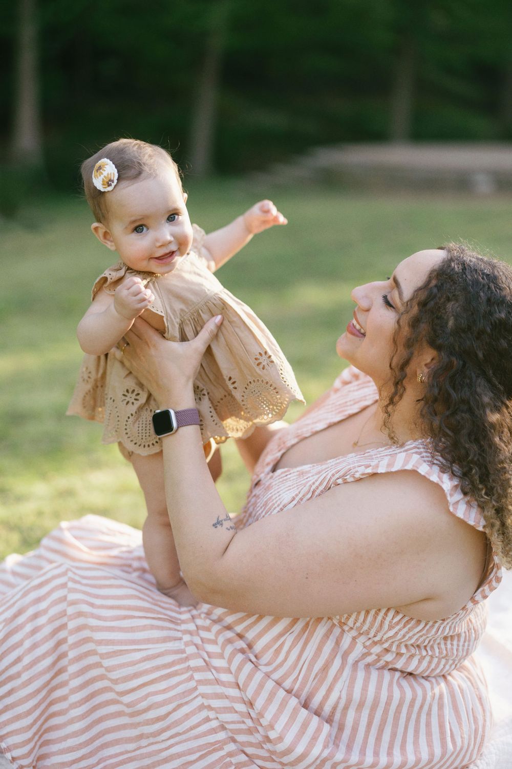 Playful moment between parent and smiling baby in matching neutral tones against green background.