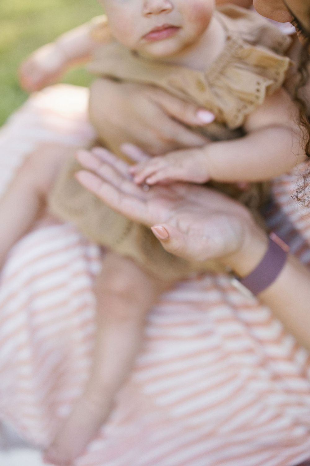 Soft focus detail shot of parent and baby's gentle moment together on striped dress.