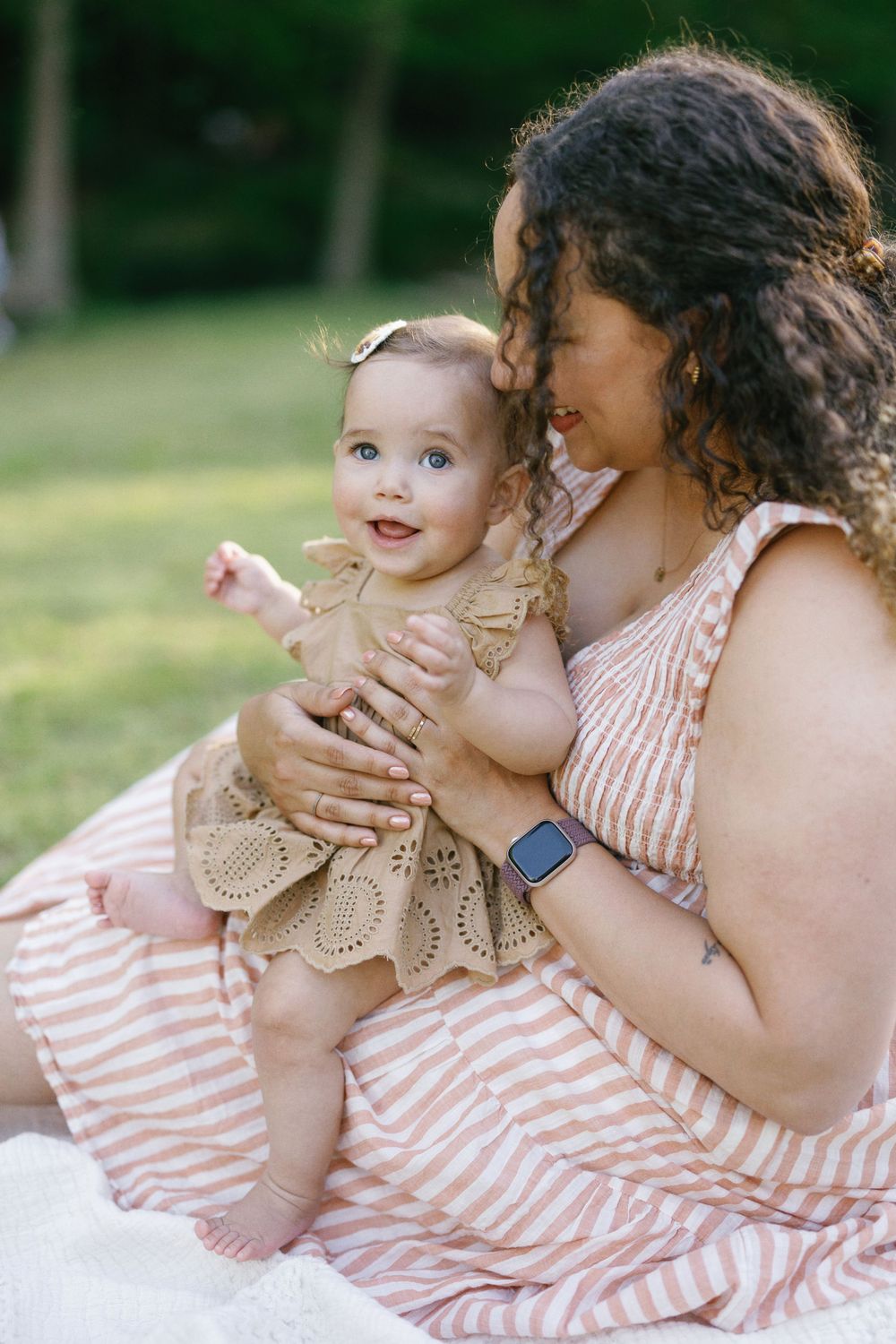 A tender outdoor moment between parent and baby wearing coordinating pink and beige outfits on a sunny day.