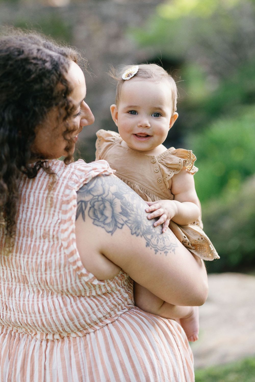A sweet interaction between parent and infant wearing a beige eyelet dress in an outdoor setting.