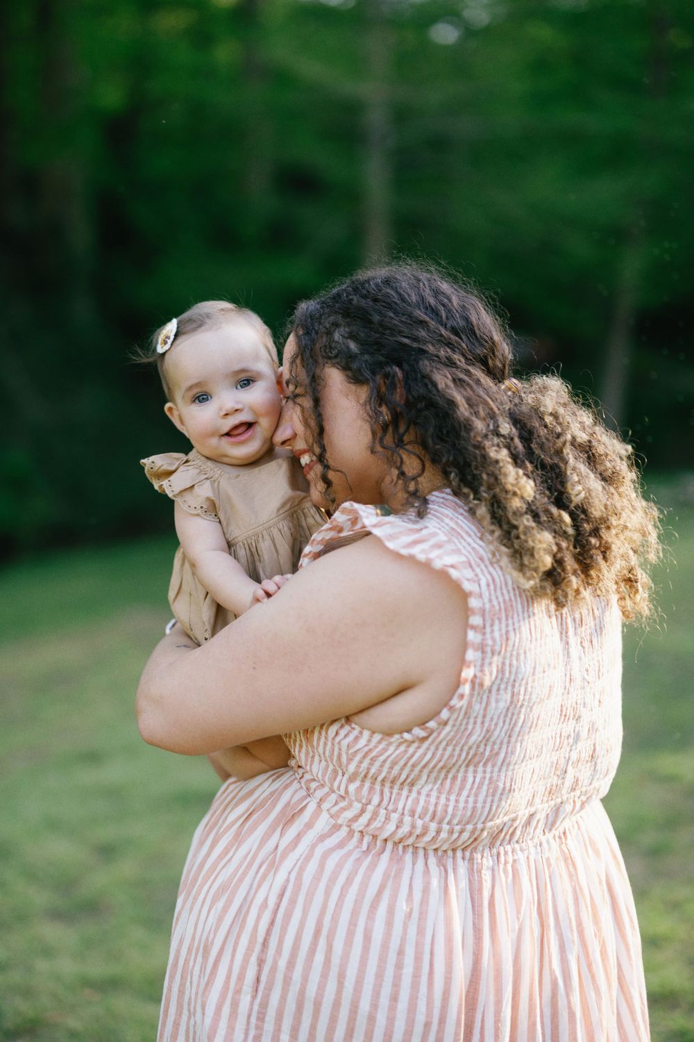 An intimate portrait of parent and baby sharing a joyful moment in a sunlit outdoor setting.