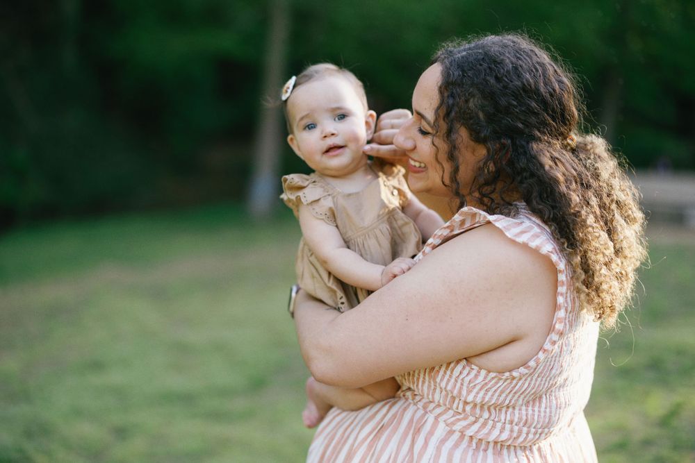 Sweet interaction between parent and infant wearing a tan dress in a natural outdoor setting.