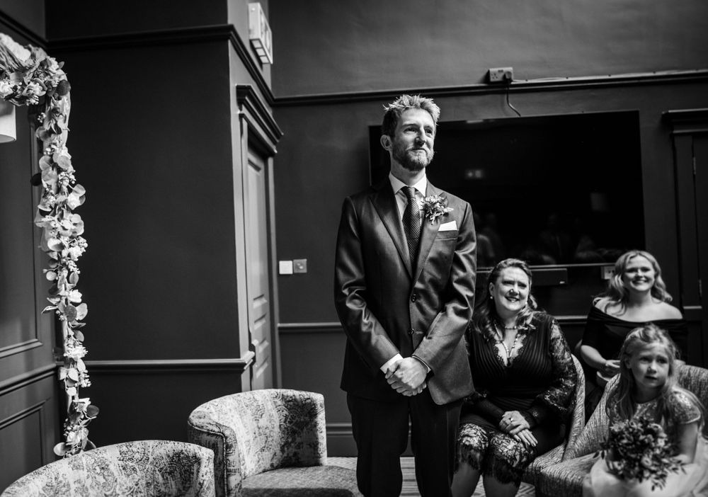A black and white image capturing a wedding ceremony moment in an elegant indoor setting with floral decor.
