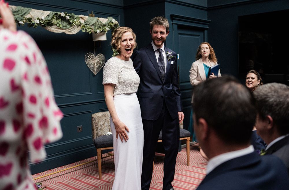A joyful wedding ceremony moment in a stylishly decorated room with dark blue walls.