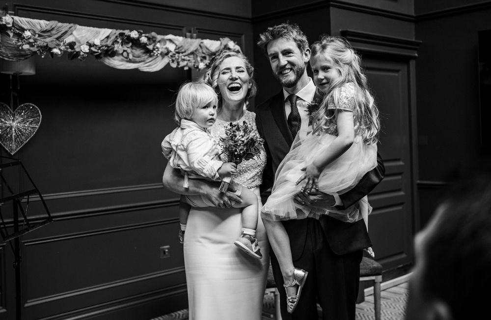 A black and white wedding portrait showing a happy moment with small children in an elegant indoor setting.