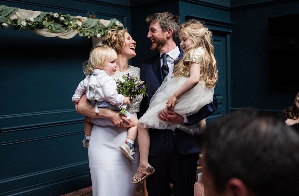 A tender family moment during a wedding celebration in a room with deep blue walls and floral garlands.