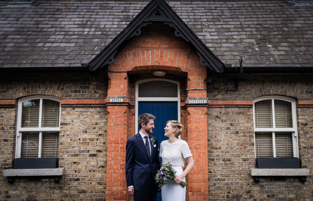 A couple poses in wedding attire against historic stone and brick architecture.
