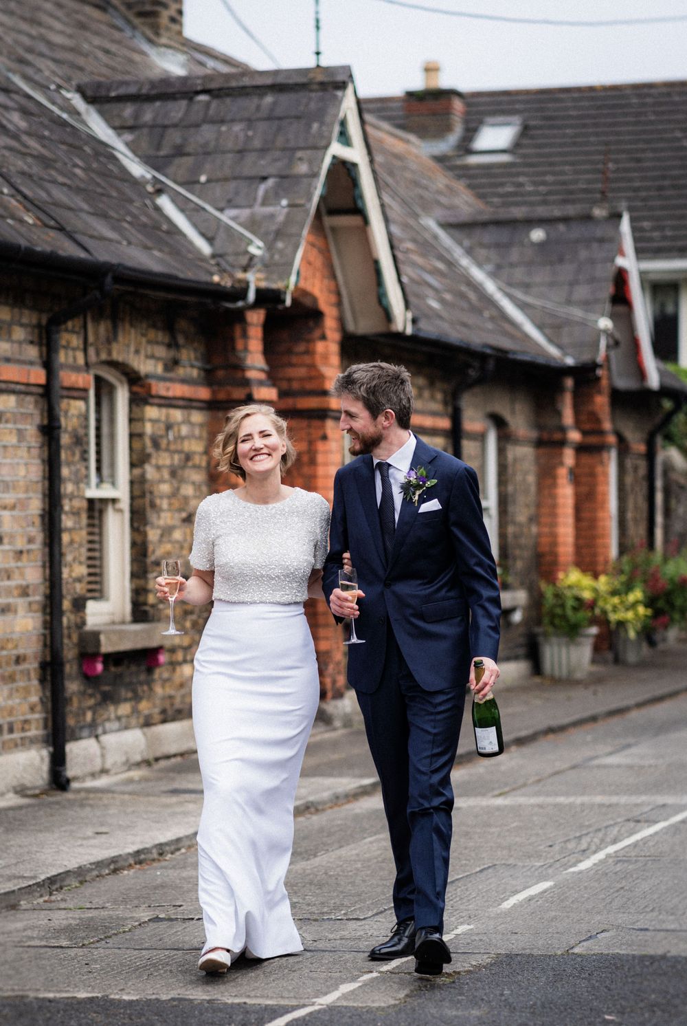 A couple walks along a charming street of historic brick houses on their wedding day.