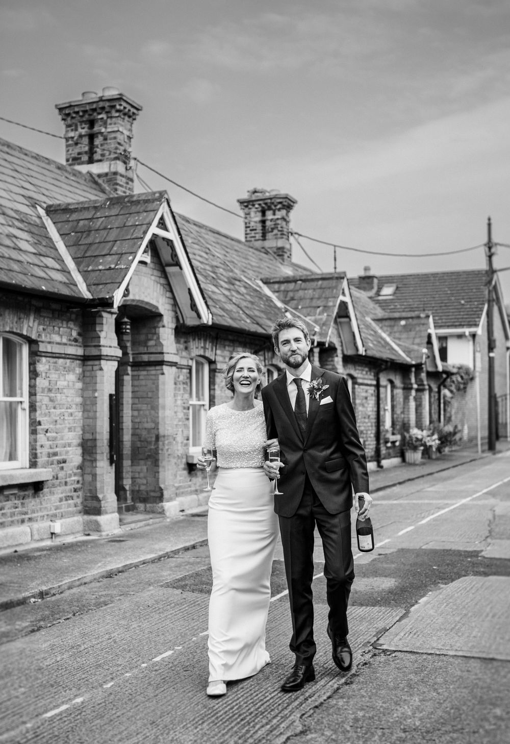 A black and white photo of newlyweds walking along a row of historic houses.